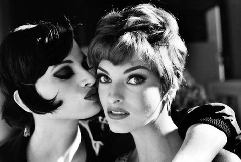 Kristen McMenamy and Linda Evangelista. 1991 Kristen McMenamy and Linda Evangelista. 1991 by Arthur Elgort, two models in short hair, one kissing the other on the cheek