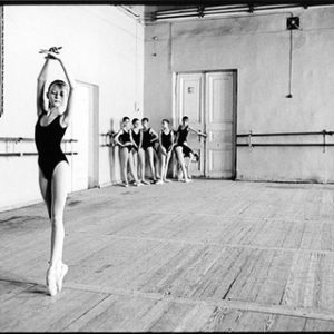 Olga by Arthur Elgort, ballerinas in black leotards, one on pointe in the front, the rest of the group aiting in a corner