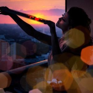 Sunset Lover by David Drebin, model on a balkony, holding a filmstrip into the sundown, lens flare