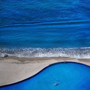 Blue Dream by David Drebin, model floating in organic shaped swimmingpool right next to the ocean