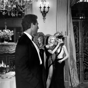 Voyeur Los Angeles by Guido Argentini, two semi nude models standing close together in a baroque interior, a man in a suit in the foreground, watching them