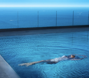 The Escapist by David Drebin, model in white swimsuit floating in a pool, the ocean in the background