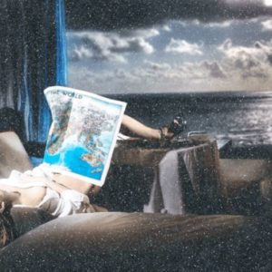 Dreaming the world by david Yarrow, model in white blouse with feet on a table and a world map in her lap, with the ocean in the background