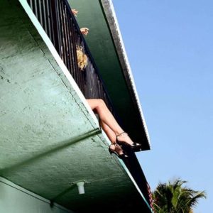 Legs by David Drebin, models legs in black heels dangeling from a green concrete balcony, a palmtree in the background