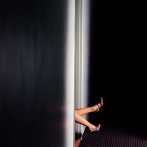 Legs in hallway by David Drebin, legs in leopard print heels sticking out of a doorway into a dark hallway