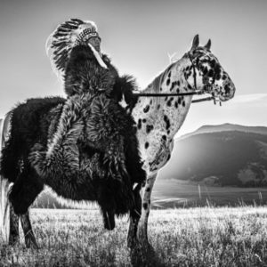 Lakota by David Yarrow, Native Chieve with feather headpiece and fur coat sitting on leopard horse