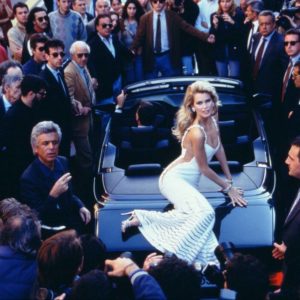 Claudia Schiffer for Valentino by Arthur Elgort, the model in white sitting on a car between men in suits